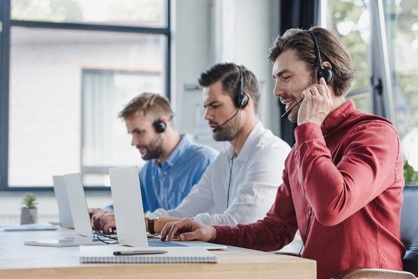 three young call center operators in headsets using laptops in office